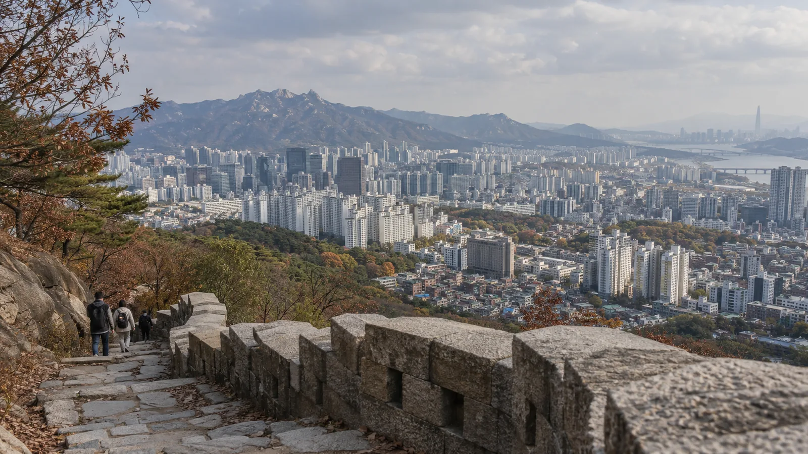 Hikers on the Seoul fortress wall trail above the city, with mountains and the Han River beyond