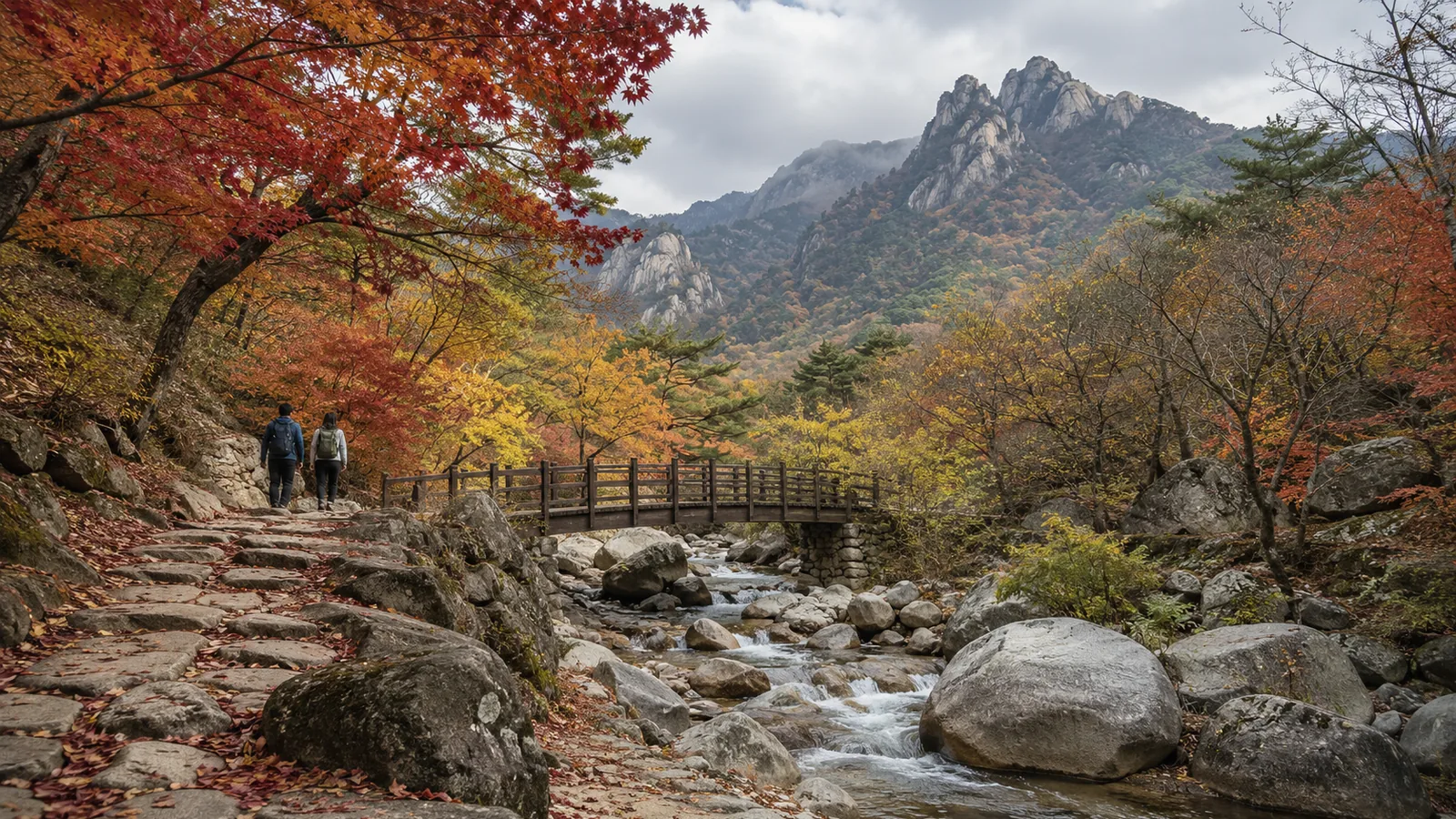 Hikers on a stone trail beside a mountain stream in red and orange autumn foliage in a Korean national park