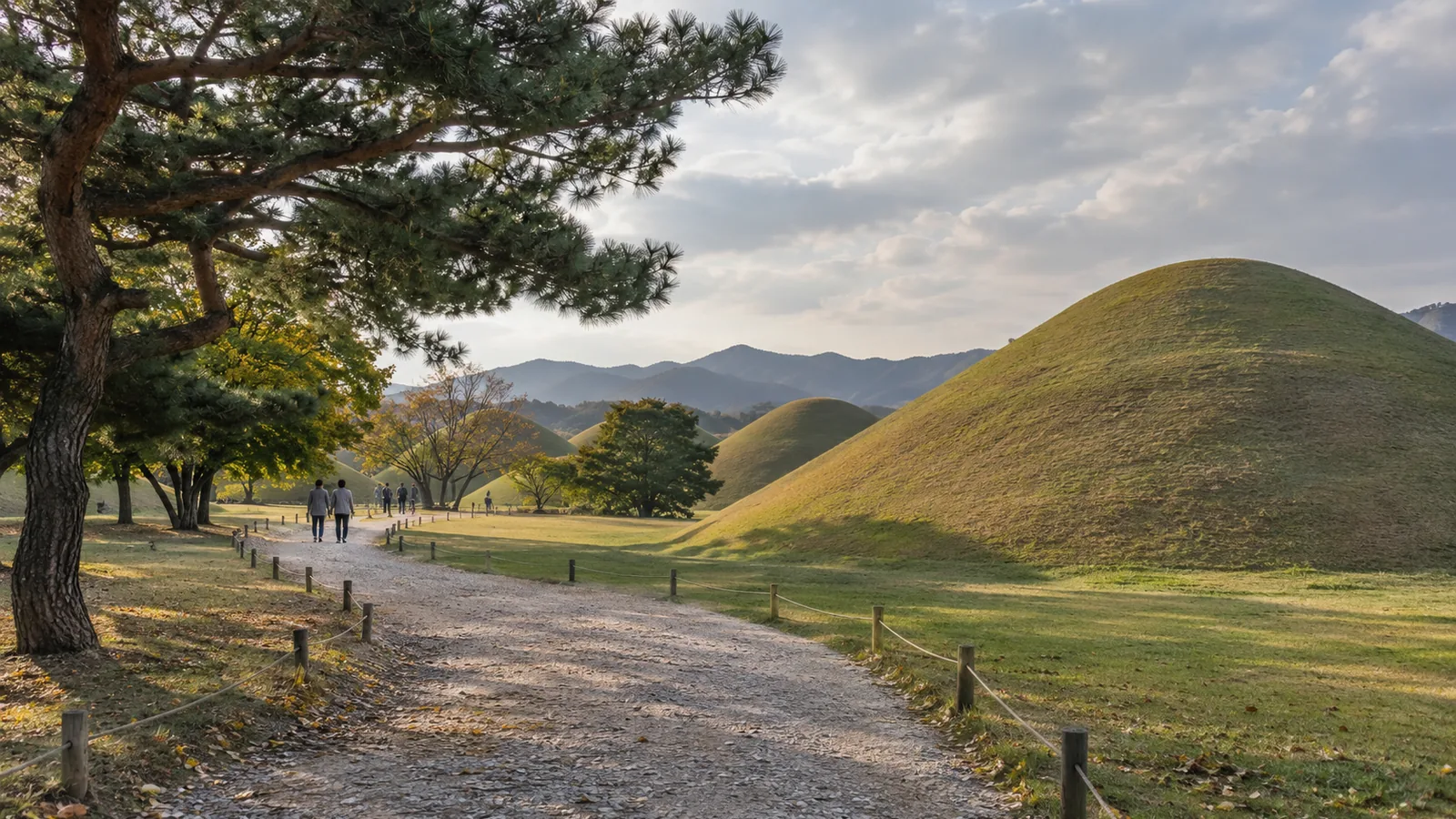 Visitors on a gravel path past grass-covered royal tombs in Gyeongju's Daereungwon tomb park
