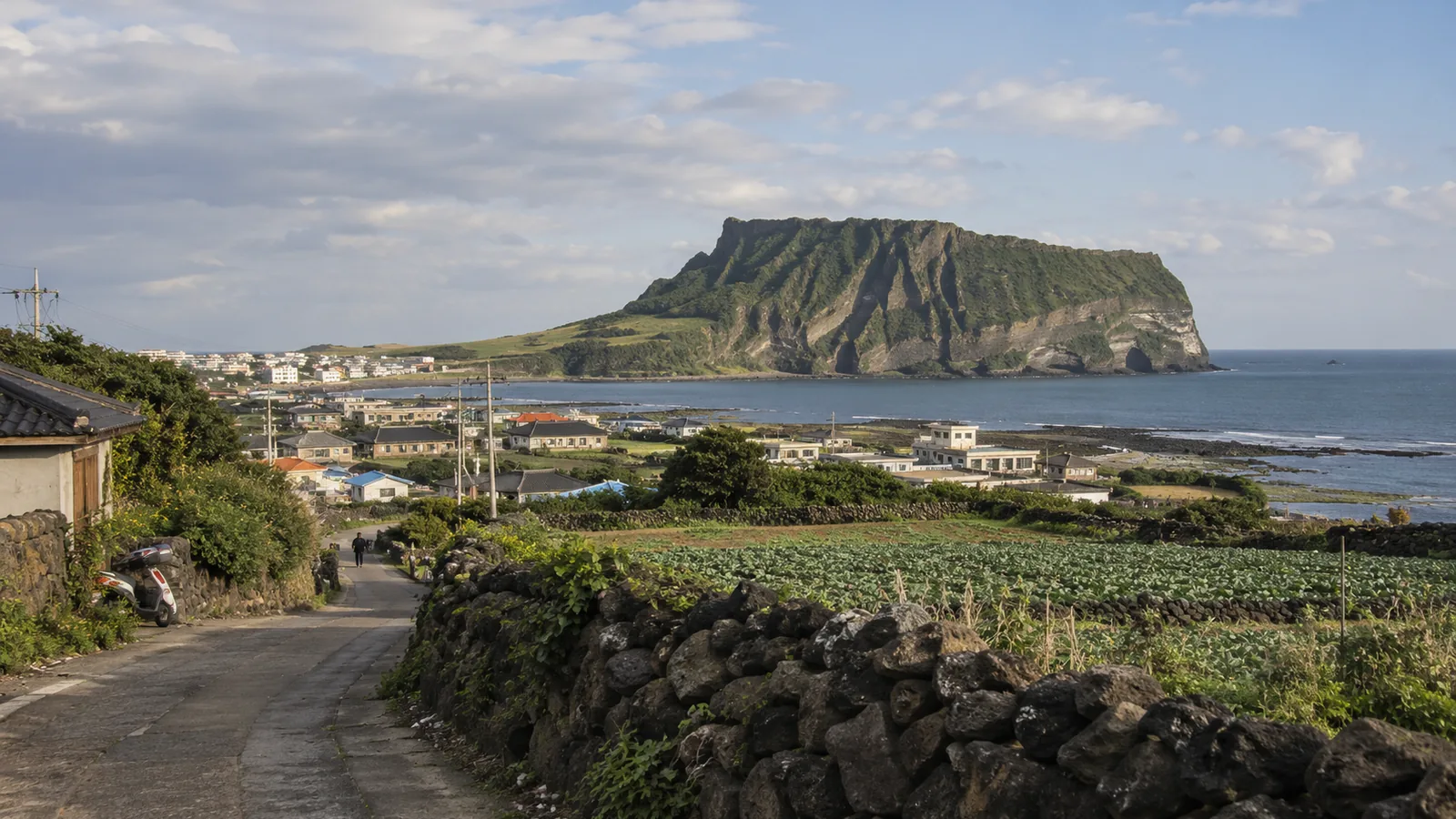 Seongsan Ilchulbong beyond a village lane with black basalt stone walls and cabbage fields on Jeju Island